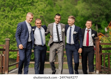 A group of five men dressed in suits and ties are posing for a photo on a bridge. Scene is lighthearted and fun, as the men are smiling and enjoying each other's company - Powered by Shutterstock