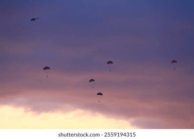 A group of five military paratroopers jumping against a bright orange and dark violet sky during sunset - Powered by Shutterstock