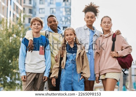 Group of five multicultural secondary school learners in casualwear standing in row in urban environment and looking at camera