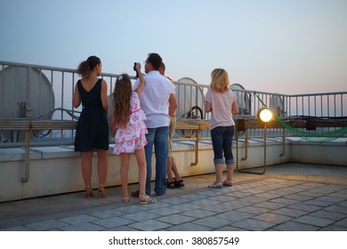 A Group Of Five People With Binoculars On The Roof Of A Multistory Building Against The Sky, View From The Back