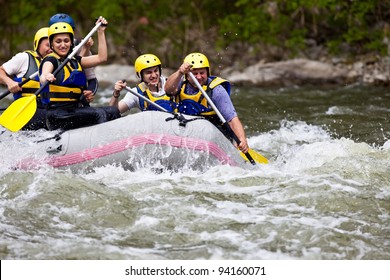 Group Of Five People Whitewater Rafting And Rowing On River