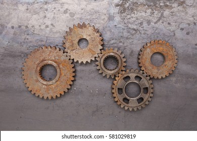 A group of five rusty gears linked together over a grungy steel background.