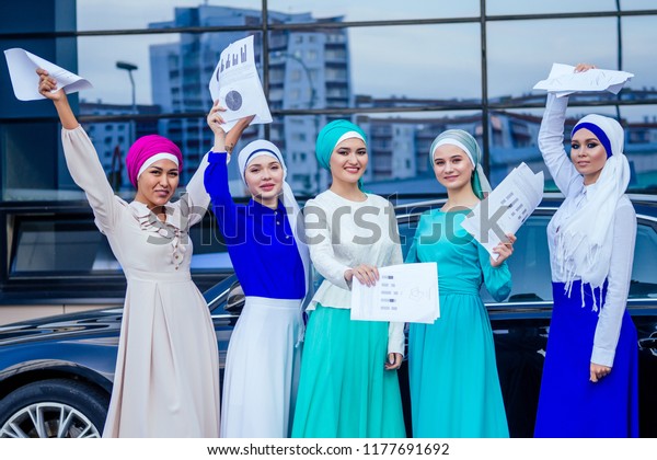 group of five strong beautiful and young Muslim\
business women fashion look stylish long dress and the turban on\
head holding paper ,car and skyscraper street background.good deal\
success teamwork
