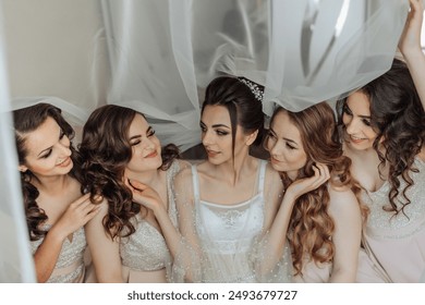 A group of five women are sitting together, with one of them wearing a wedding dress. The women are smiling and seem to be enjoying each other's company - Powered by Shutterstock