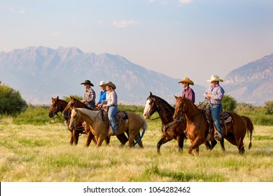 A group of five young people horseback riding in the grassy fields with the mountains of Utah in background