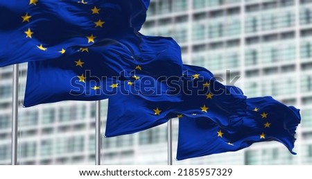 group of flags of the European Union waving in the wind in front of the European Parliament building.