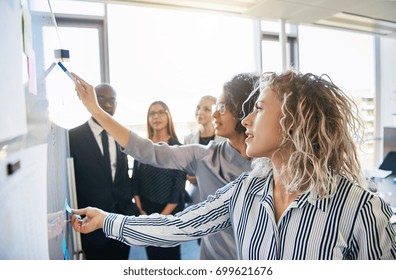 Group Of Focused Business Colleagues Brainstorming Together On A Whiteboard During A Strategy Session In A Bright Modern Office