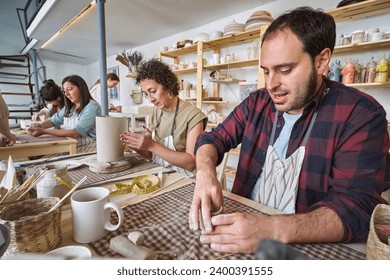  A group of focused individuals crafting pottery in a bright, organized studio, surrounded by shelves of ceramic pieces - Powered by Shutterstock