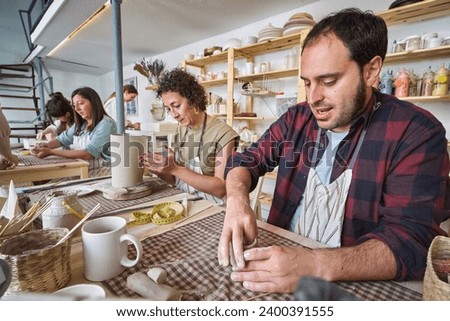  A group of focused individuals crafting pottery in a bright, organized studio, surrounded by shelves of ceramic pieces