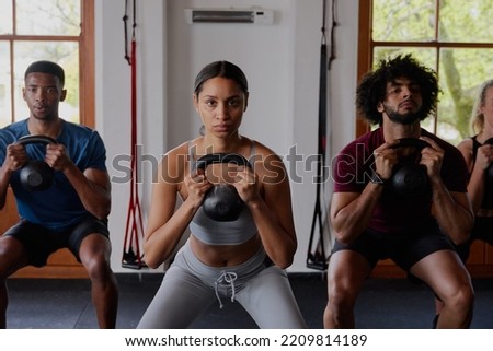 Group of focused multiracial young adults doing kettlebell squats at the gym