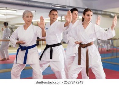 Group of focused people wearing white kimonos standing in attacking stance, practicing movements of close combat punches in training room during martial arts workout.. - Powered by Shutterstock