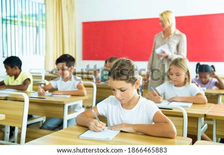 Group of focused pupils sitting at classroom working at class with teacher