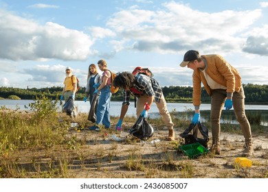 A group of focused volunteers diligently clears litter from a picturesque lakeshore under a cloudy sky. Active Volunteers Participating in a Lakeshore Cleanup Campaign. High quality photo - Powered by Shutterstock