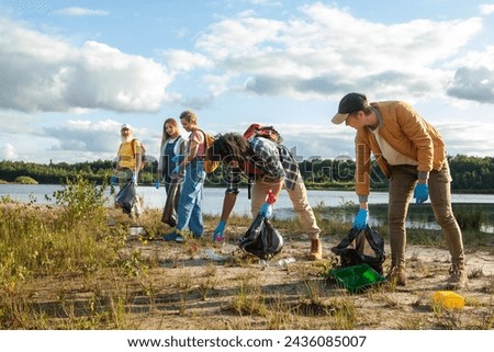A group of focused volunteers diligently clears litter from a picturesque lakeshore under a cloudy sky. Active Volunteers Participating in a Lakeshore Cleanup Campaign. High quality photo