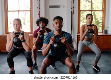 Group of focused young adults doing kettlebell squats at the gym - Powered by Shutterstock