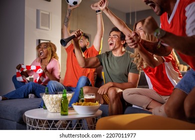 Group of football fans cheering while watching game on TV, celebrating their team scoring a goal and winning the match. Focus on the hand holding football cheering horn - Powered by Shutterstock