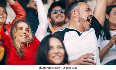 Group Of Football Fans Watching A Sport Event And Cheering. Excited Crowd Of Sports Fans Cheering In Stadium.