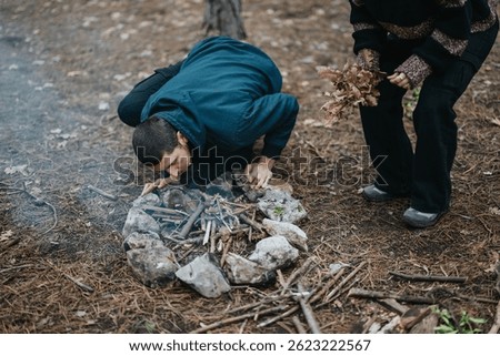 Group in a forest setting starting a campfire, embodying outdoor adventure, teamwork, and preparation on a serene winter outing.