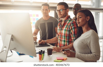 Group Of Four Black, Caucasian And Hispanic Adult Entrepreneurs Wearing Casual Clothing While Standing Around Computer For Demonstration Or Presentation