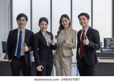 A group of four business professionals giving thumbs up in a modern office setting, symbolizing teamwork and success. - Powered by Shutterstock