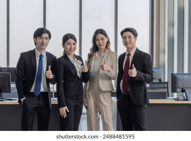 A group of four business professionals giving thumbs up in a modern office setting, symbolizing teamwork and success. - Powered by Shutterstock