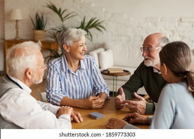 Group Of Four Cheerful Senior Friends, Two Men And Two Women, Sitting At Table And Enjoying Talk After Playing Cards In Assisted Living Home