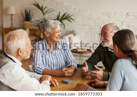 Group of four cheerful senior friends, two men and two women, sitting at table and enjoying talk after playing cards in assisted living home