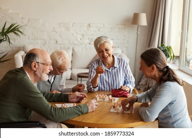 Group Of Four Cheerful Senior People, Two Men And Two Women, Having Fun Sitting At Table And Playing Bingo Game In Nursing Home