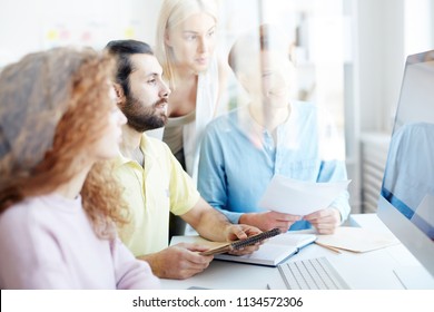 Group Of Four Creative People Watching Webcast For Designers While Sitting In Front Of Computer Monitor