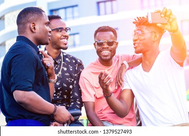 A Group Of Four Fashionable Cool African American Guys Students Communicating On The Street Looking At Smartphone Take Pictures Selfie On Phone