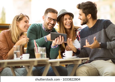 Group of four friends having a coffee together. Two women and two men at cafe talking laughing and enjoying their time using digital tablet. - Shutterstock ID 1033822804