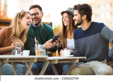 Group of four friends having a coffee together. Two women and two men at cafe talking laughing and enjoying their time using digital tablet. - Shutterstock ID 1183623769