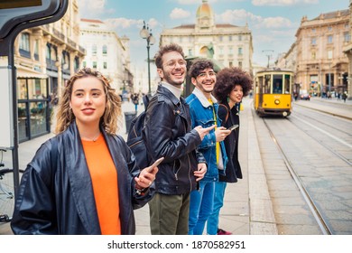 Group of four friends multiethnic men and women waiting smiling at bus stop commuting using smartphone handhold - Powered by Shutterstock