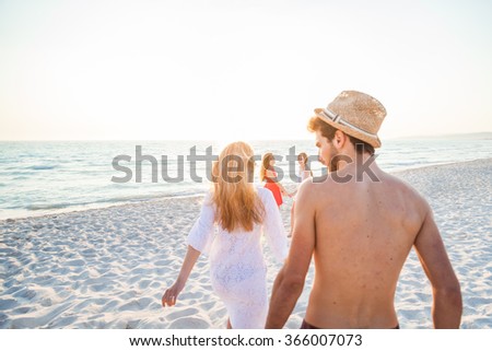 A group of four friends walking on the beach at sunset. One young men and three young women in small groups, they walking on the sand in a day of rest. Two women holding hands