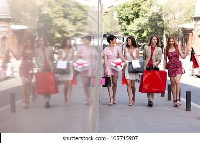 Group of four happy fashionable friends walking on the street smiling and holding colorful shopping bags.