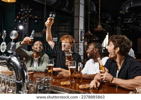group of four happy multiethnic male friends raising glasses of beer at bar counter, bachelor party