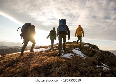 Gruppe von vier Wanderer mit Rucksäcken wandert bei Sonnenuntergang in die Berge