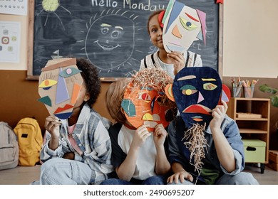 Group of four kids in classroom holding handmade cardboard abstract faces presenting art project results - Powered by Shutterstock