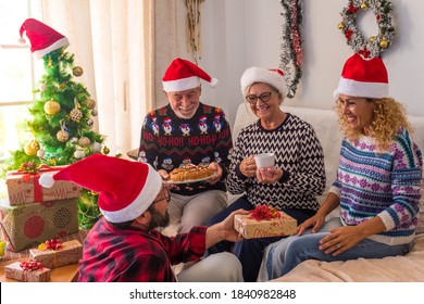 Group Of Four Mature And Young People Having Fun At Home The Christmas Day Wrapping The Presents And Gifts Together - Man Giving At His Woman A Gift