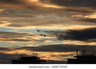 A group of four military paratroopers jumping against a bright orange and dark sky during sunset above a city - Powered by Shutterstock