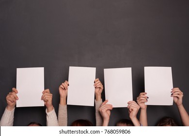 Group Of Four People Holding Paper Sheets Above Heads On Gray Background. Mockup Template For Team Work In Business Concept