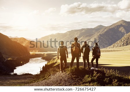 Group of four people stands on mountains and river backdrop. Travel expedition trekking concept with space for text