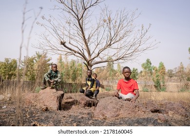 Group of four sad looking African boys sitting on a dried up farm doing nothing; crop failures, job losses, rising food prices, food speculation and poverty due to climate change