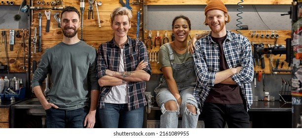 Group of four smiling multiethnic cycling technicians posing and looking at camera at workplace in modern bicycle workshop. Young guys and girls. Friendship. Teamwork. Bike service, repair and upgrade - Powered by Shutterstock