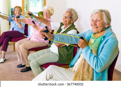 Group of four smiling senior women toning their arms with elastic strengthening bands while seated in fitness class - Powered by Shutterstock