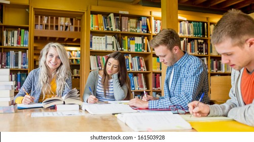 Group Of Four Students Writing Notes At Desk In The College Library