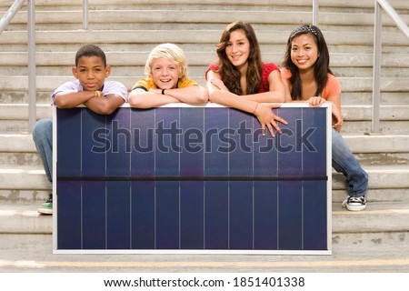 Group of four teenagers of mixed ethnicities posing with a solar panel to promote the use of alternate sources of energy