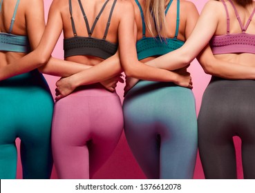 Group Of Four Women Buttocks In Blue Gray And Brown Sport Wear Standing Together After Workout On Pink Background