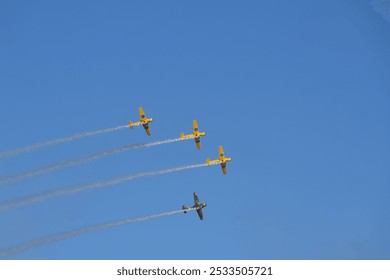 A group of four yellow airplanes performing a formation flight against a clear blue sky. - Powered by Shutterstock