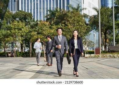 group of four young asian business people walking outdoors on street in modern city
